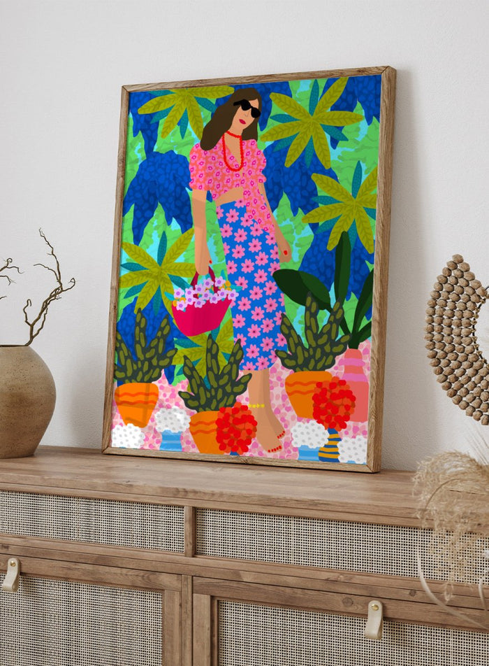 Woman in a floral dress holding a basket of flowers amidst colorful plants. Walking Between Gardens by Rafaela Mascaro fine art print poster featuring woman carrying flowers in lush tropical garden, modern contemporary botanical wall art.