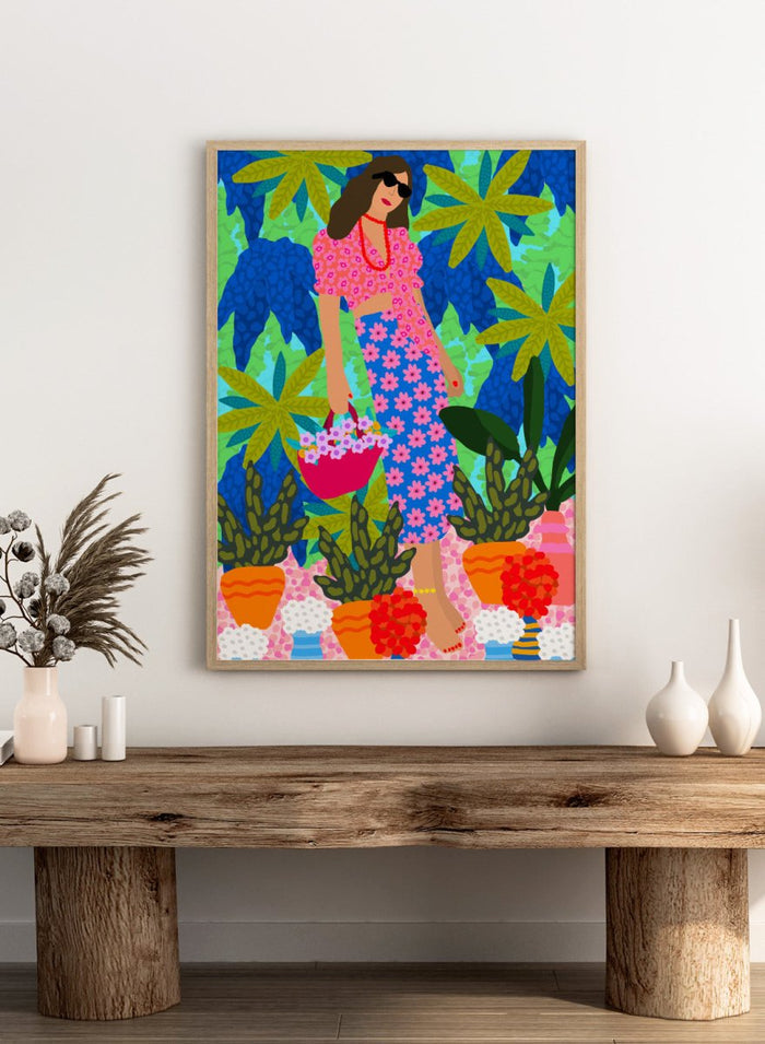 Woman in a floral dress holding a basket of flowers amidst colorful plants. Walking Between Gardens by Rafaela Mascaro fine art print poster featuring woman carrying flowers in lush tropical garden, modern contemporary botanical wall art.