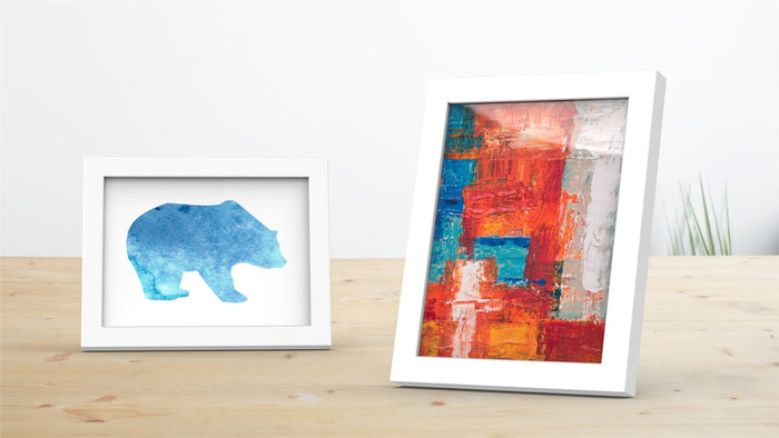Two white picture and poster frames displaying blue bear silhouette and colorful abstract artwork.