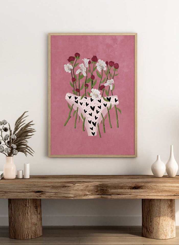 White underwear with black heart patterns surrounded by flowers on a pink background. Blooming Slip by Raissa Oltmanns features a feminist illustration of flowers growing from heart-patterned underwear on a pink background. Bold floral art print with strong feminine symbolism.