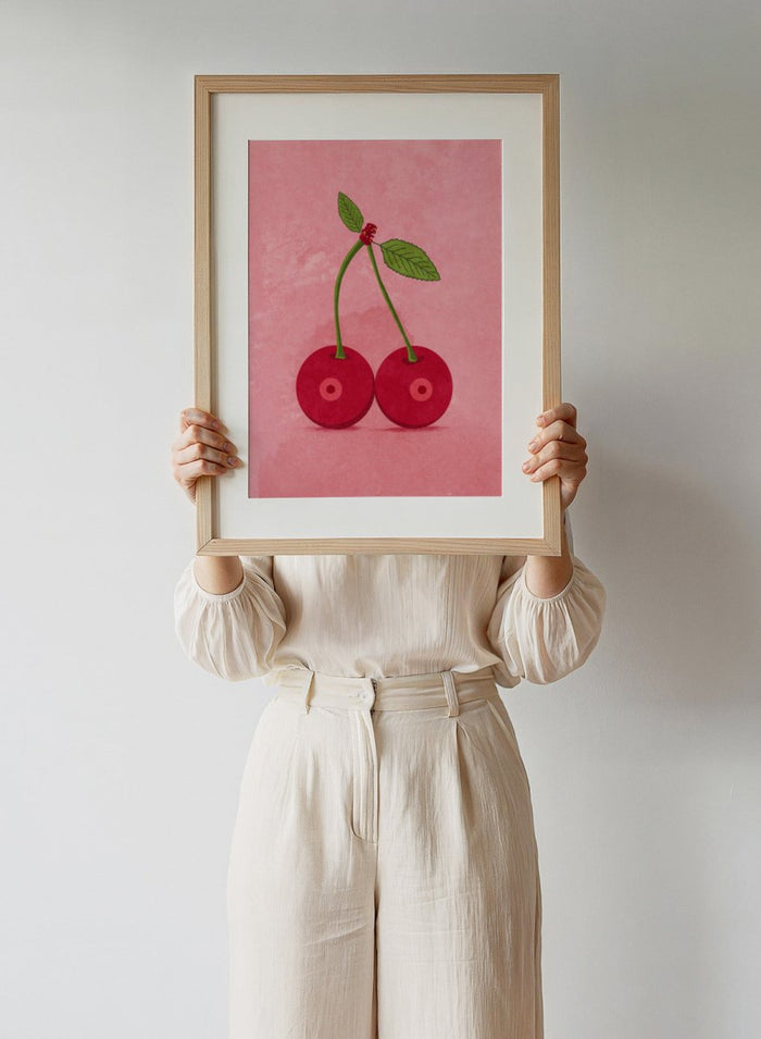 Illustration of two cherries on a pink background. Cherry Boobs by Raissa Oltmanns is a modern pop art fine art print featuring red cherries illustration and bold playful contemporary wall decor poster.