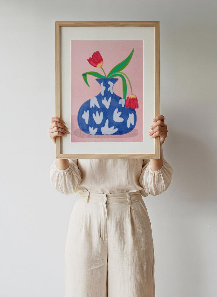 Blue vase with white abstract patterns and red tulips on a pink background. Tulip in Vase by Raissa Oltmanns fine art print featuring bold red tulip, blue patterned vase, modern contemporary floral wall decor poster.