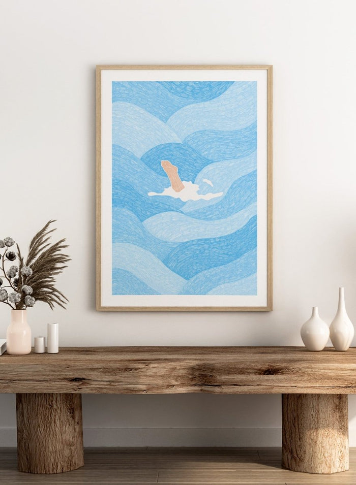 Illustration of a person swimming in blue water with a white border. Hand Reaching Blue Ocean by Rio Soléy is a modern coastal art print featuring swirling blue waves, minimalist illustration, playful design, and contemporary seaside charm.