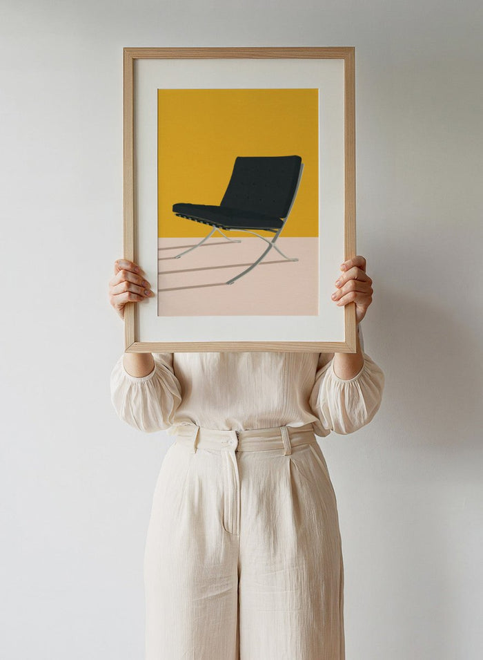 Black chair with metal legs on a yellow and beige background. Barcelona Chair by Mies Van Der Rohe by Rosi Feist is a minimalist modern design art print featuring clean lines and bold color. Officially licensed fine art poster with optional real wood framing, ready to hang.