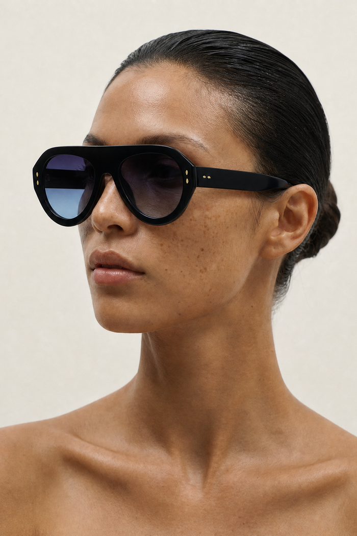 Woman wearing large black AVIATOR  sunglasses against a plain background