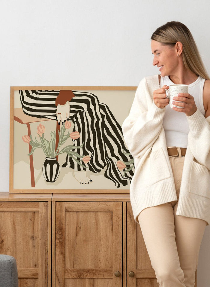 Artistic depiction of a person with striped pants sitting on a chair with floral arrangements. Tulips By My Feet by Sannel Larson is a modern minimalist art print with woman in striped pants and soft tulips. Officially licensed wall poster with framing.