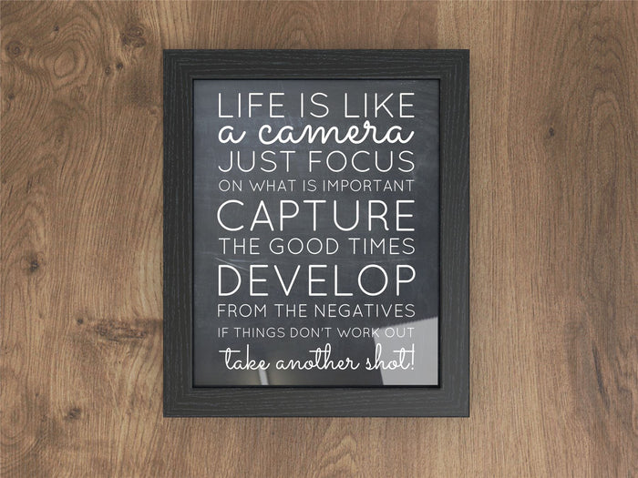 Black picture and poster frame displaying inspiring photography quote on a wooden background.