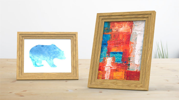 Verona Range oak picture and poster frame displaying a blue bear illustration and vibrant abstract art on a wooden table.