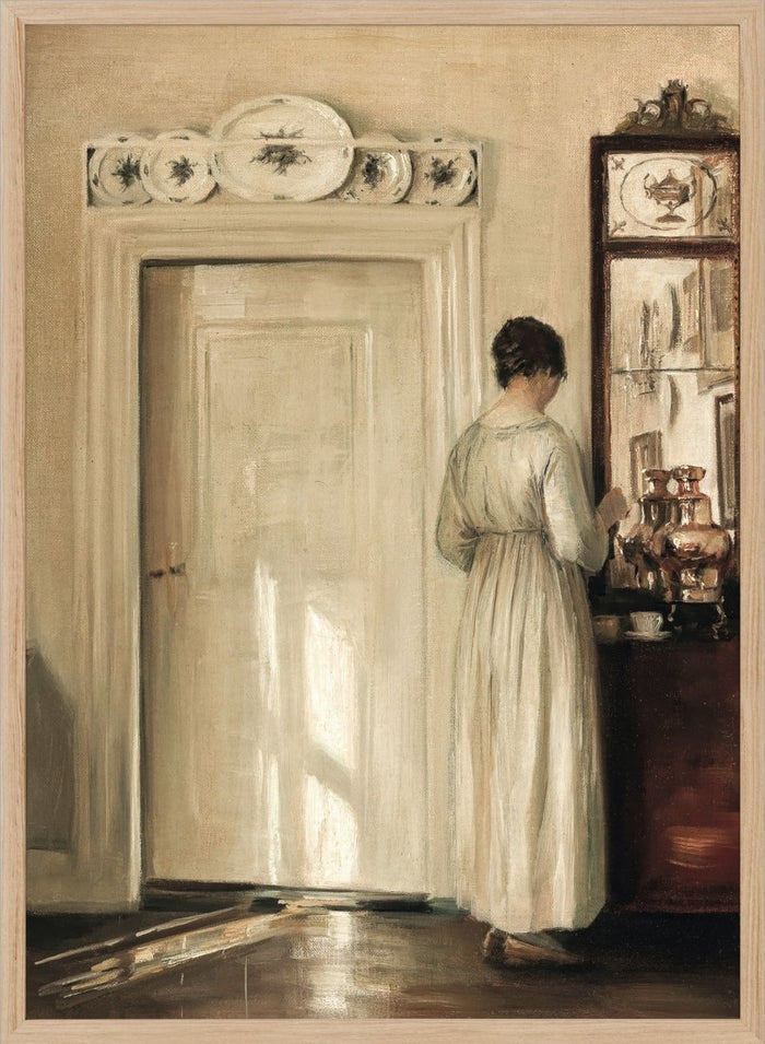 Woman in a white dress standing in a room with a door and shelves filled with items. Woman Making Tea by Carl Holsøe is a vintage Danish interior art print featuring Scandinavian home interiors, muted tones, natural light, and a woman preparing tea.