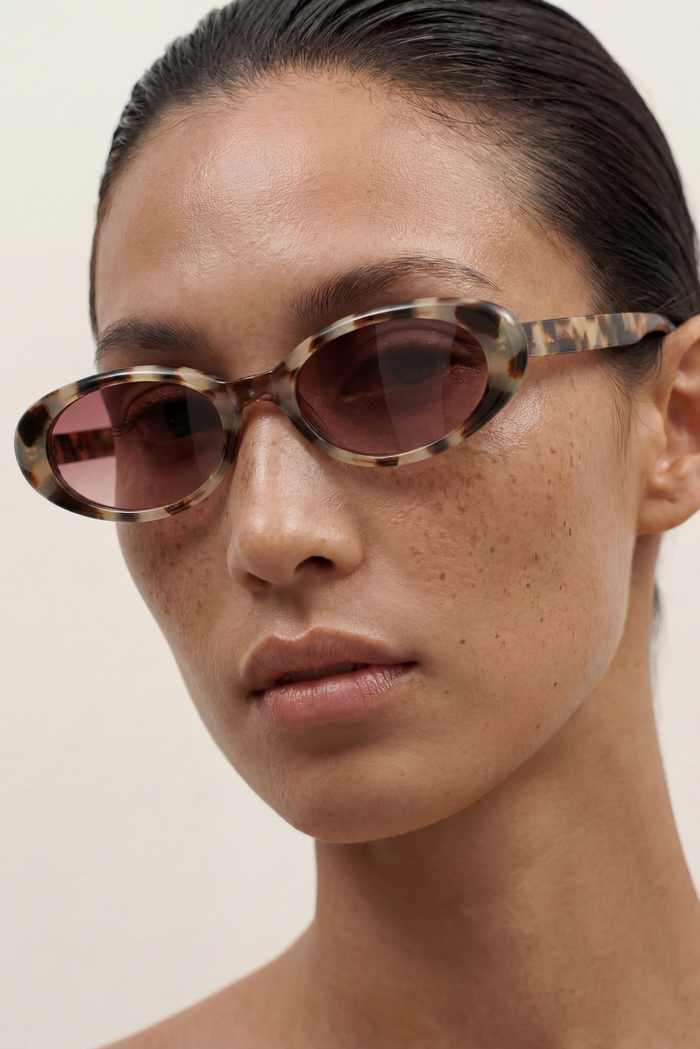 Close-up of a person wearing tortoiseshell sunglasses with a neutral background